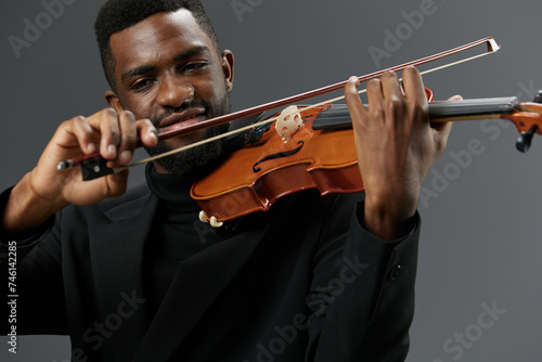 A talented African American musician in a sleek black suit playing a violin on a neutral gray background