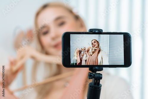 Young social medial content creator woman make fashion video. Blogger smiles and using phone stick selfie while making persuasive online clothing sell vlog to audience or follower. Blithe