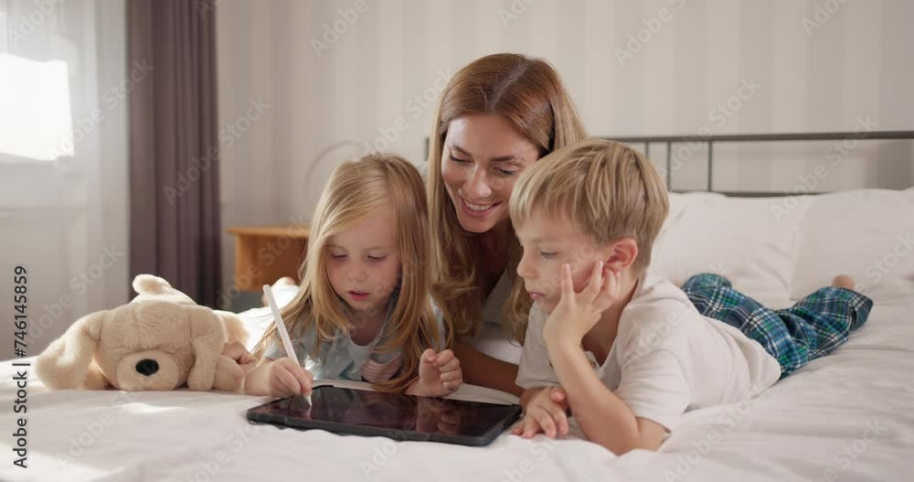 Cute children coloring on a digital tablet with mother in bedroom Cute children coloring on a digital tablet with mother in bedroom