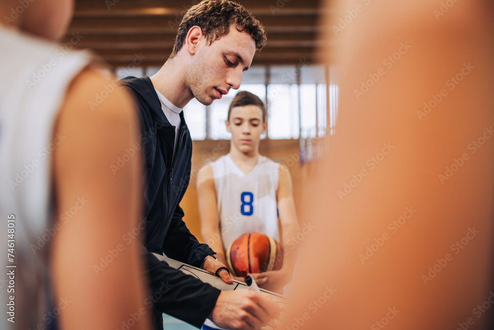 A young basketball coach is working on tactics with his junior team. A young basketball coach is working on tactics with his junior team.