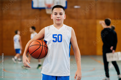 Portrait of a basketball kid posing with a ball on court during training. © Zamrznuti tonovi