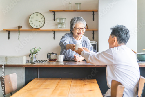 キッチンからコーヒーを渡すシニアの女性・妻・奥さんコーヒーを受け取るシニアの男性・夫
 photo