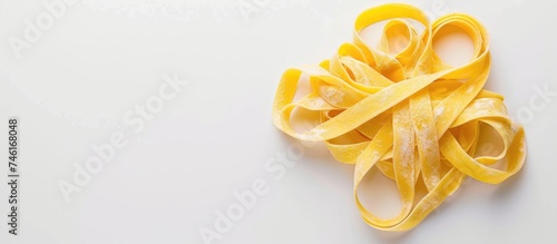 A heap of triangle-shaped homemade fettuccine nestles on a clean white surface, showcasing the vibrant yellow color of the pasta. Each strand is carefully arranged to form a visually appealing