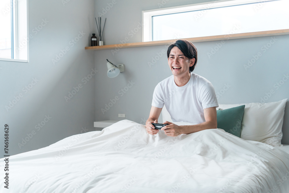 Obraz premium 家のベッドルーム・寝室でゲームをする男性ゲーマー(不摂生・遊ぶ・ストレス解消)