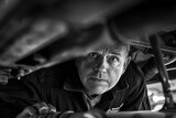 Engrossed mechanic working under a car, with a focused expression, highlighting expertise and precision in a monochrome tone.

