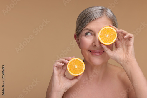 Beautiful woman with halves of orange rich in vitamin C on beige background, space for text