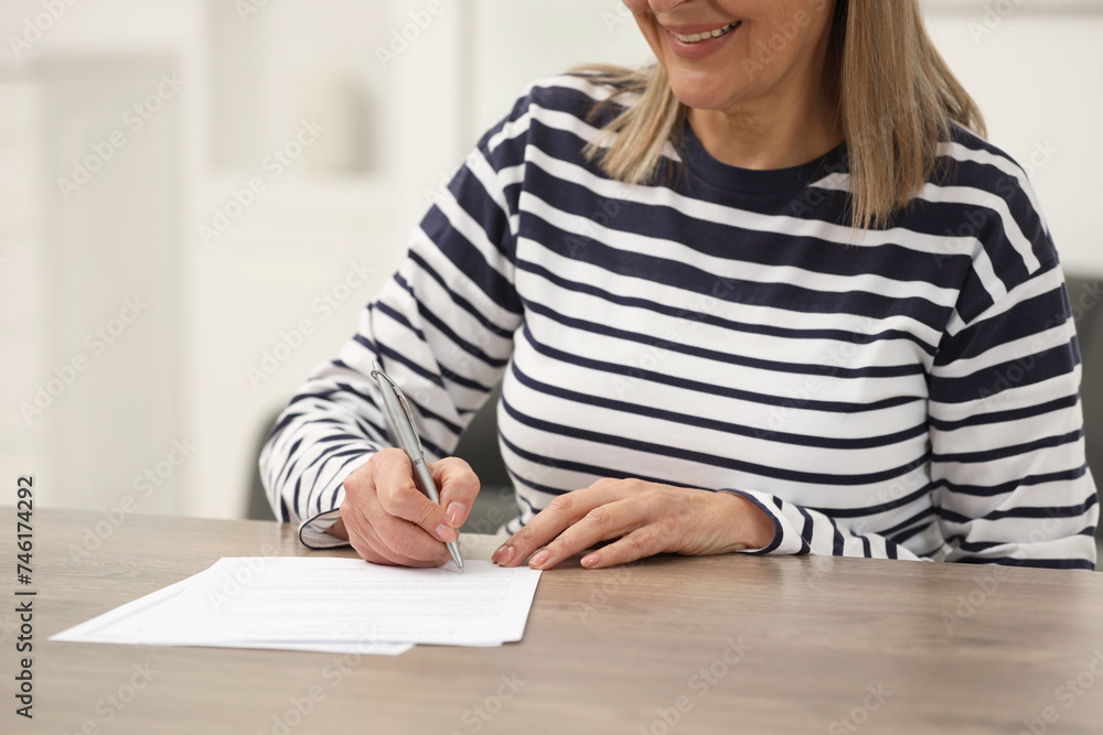 Smiling senior woman signing Last Will and Testament at wooden table indoors, closeup Smiling senior woman signing Last Will and Testament at wooden table indoors, closeup
