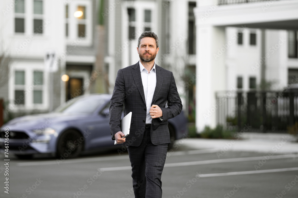Businessman walking in city. Gray hair business man walk on city street. Business man walking outdoor, hold laptop. Business man in suit go to office work. Successful business. Businessman walking in city. Gray hair business man walk on city street. Business man walking outdoor, hold laptop. Business man in suit go to office work. Successful business.