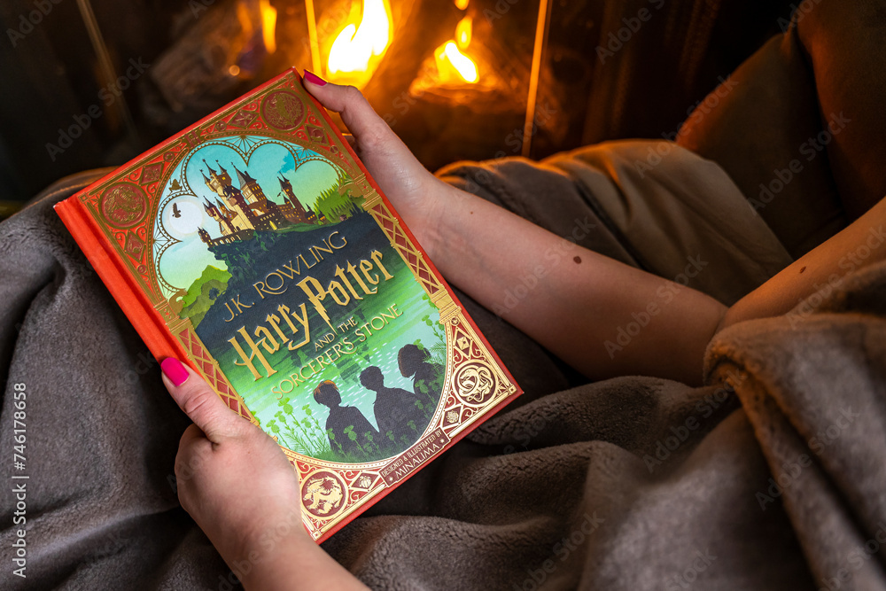 Naklejka premium Teenage girl reading the first book about Harry Potter near the fireplace. 