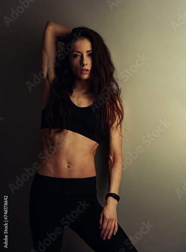 Sport sexy body beautiful slim woman with long hair posing in black sport bra showing the shoulders, abs, arms, standing on studio wall background with empty copy space. Healthy lifestyle