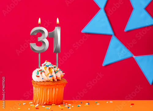 Birthday cupcake with candle number 31 on a red background with blue pennants