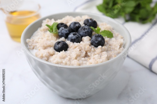 Delicious barley porridge with blueberries and mint in bowl on white marble table, closeup