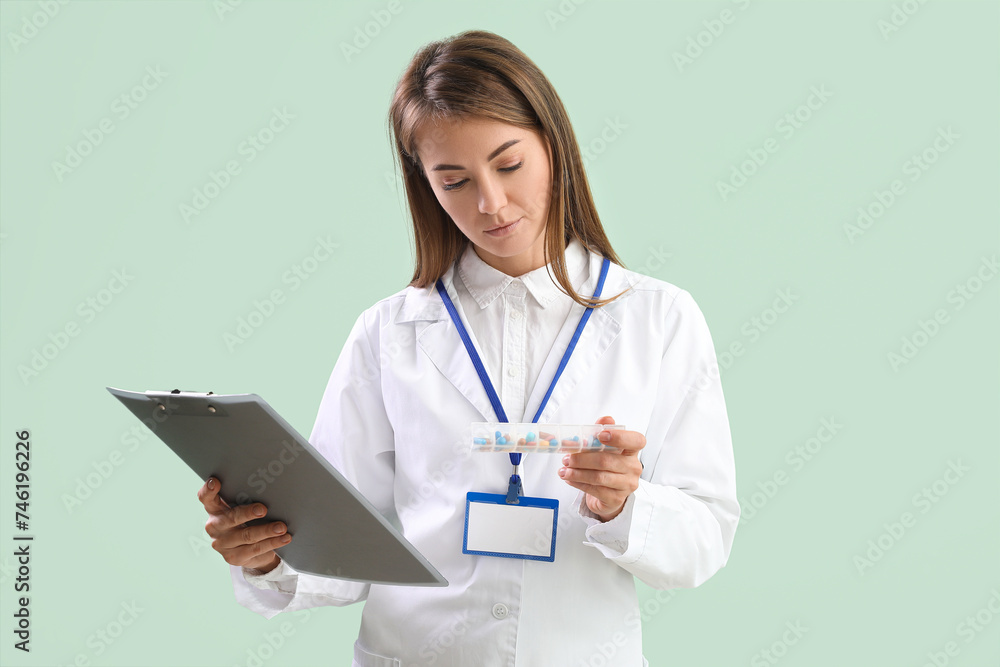 Female doctor with container of vitamin supplements and clipboard on green background Female doctor with container of vitamin supplements and clipboard on green background