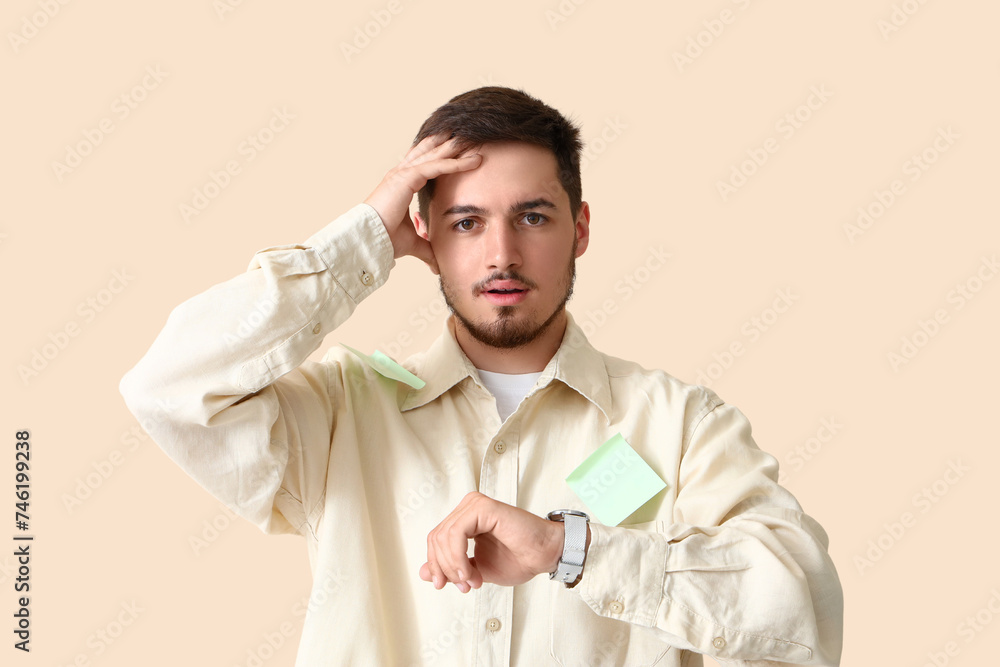 Stressed young man looking at wristwatch on beige background. Deadline concept Stressed young man looking at wristwatch on beige background. Deadline concept