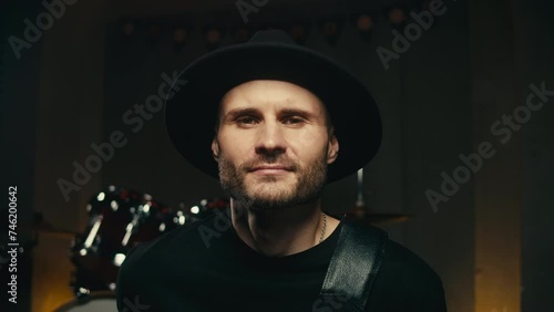 Young man in black hat with moustache and beard portrait. Musician man in music studio with guitar in hands close-up photo