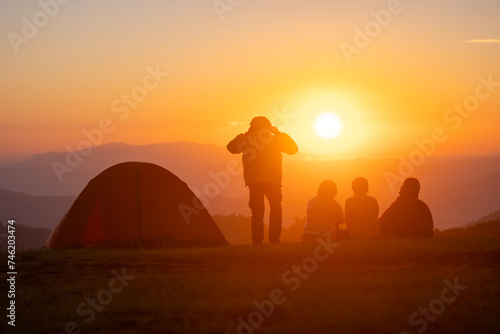 Group of friends sitting by the tent during overnight camping while looking at the beautiful view point sunset over the mountain for outdoor adventure vacation travel concept