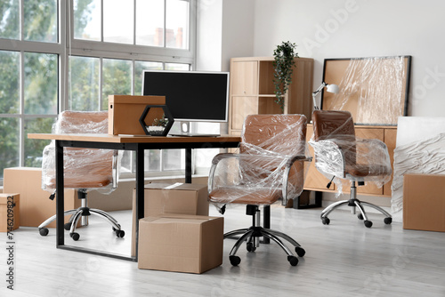 Interior of modern office with chairs wrapped in stretch film and cardboard boxes on moving day photo