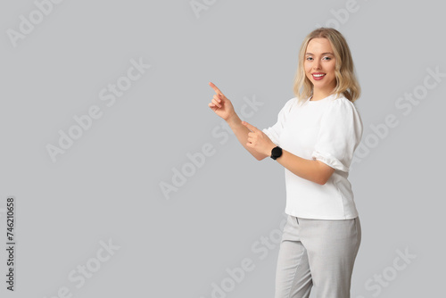 Pretty young woman with modern smartwatch pointing at something on grey background