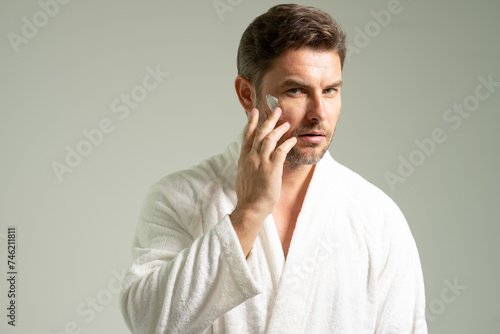 Beauty, skincare and man with cream on face using skincare products, lotion. Closeup of male face. Men's beauty. man is applying moisturizing and anti aging cream on his face against white background.