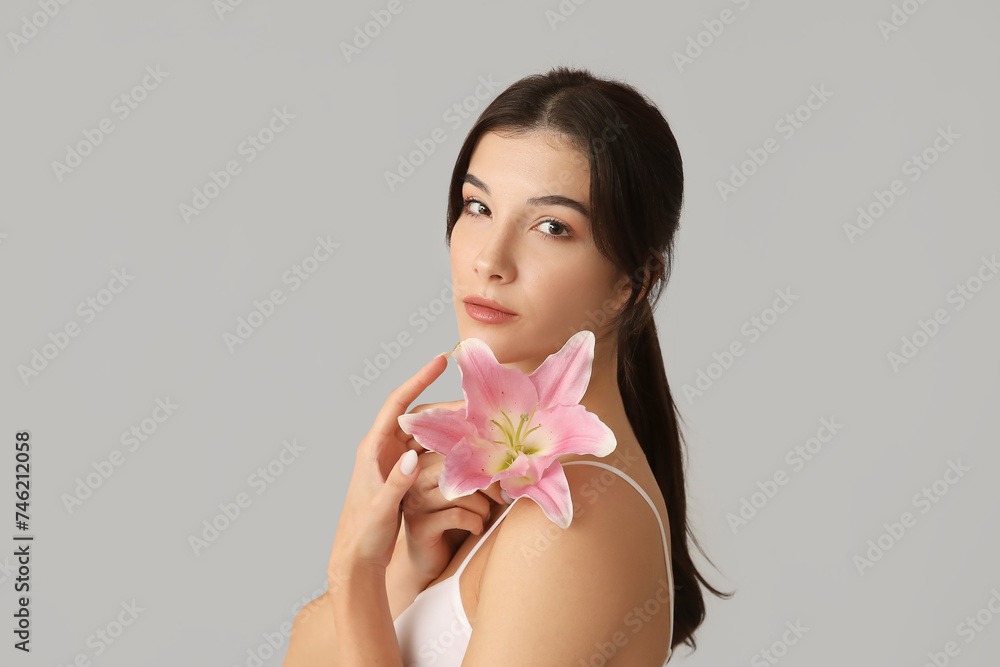 Beautiful young woman with pink lily flower on grey background Beautiful young woman with pink lily flower on grey background