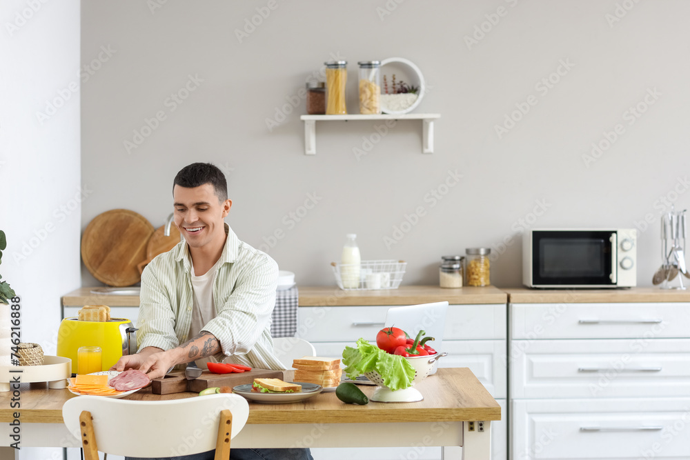 Young man preparing ingredients for tasty sandwich in kitchen Young man preparing ingredients for tasty sandwich in kitchen