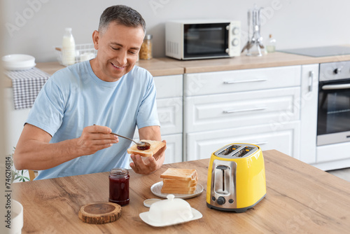 Middle-aged man having sweet jam toasts for breakfast in kitchen