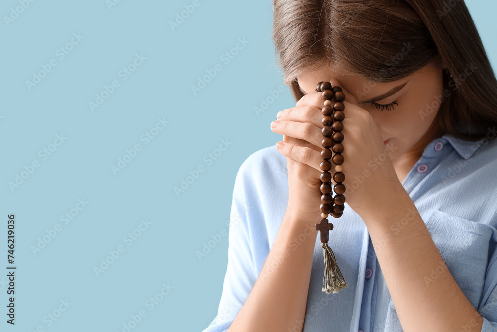 Young woman praying with beads on blue background, closeup