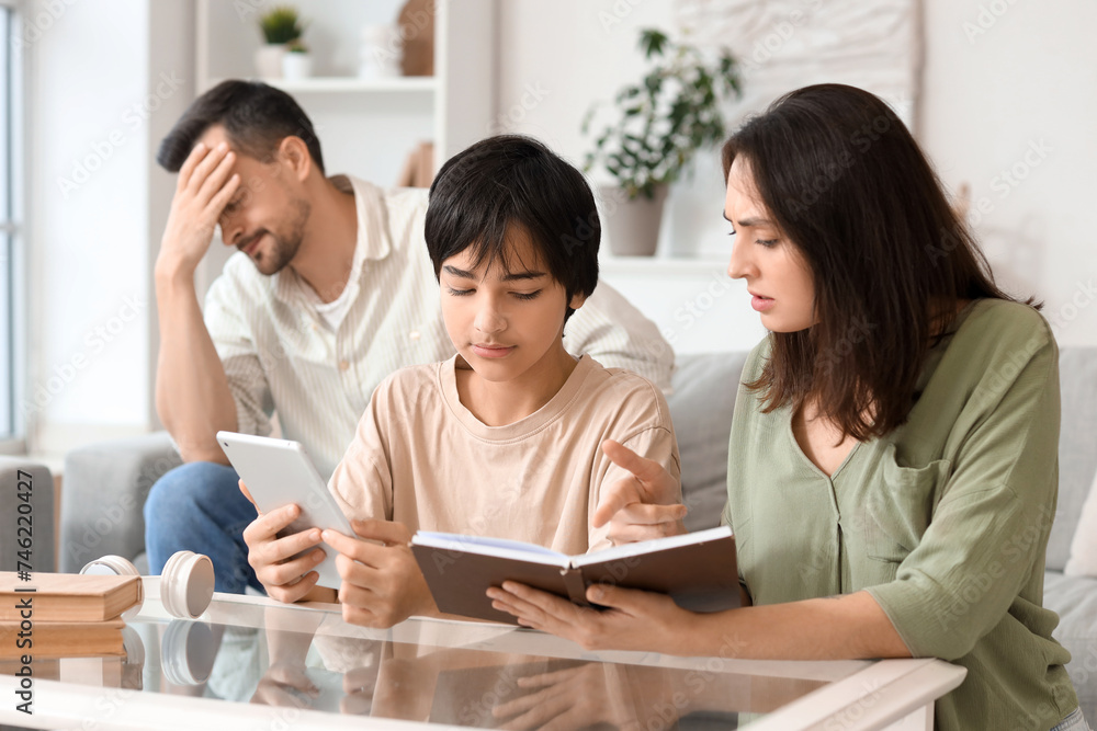 Teenage boy with tablet computer and his mother showing book at home. Family problem concept Teenage boy with tablet computer and his mother showing book at home. Family problem concept