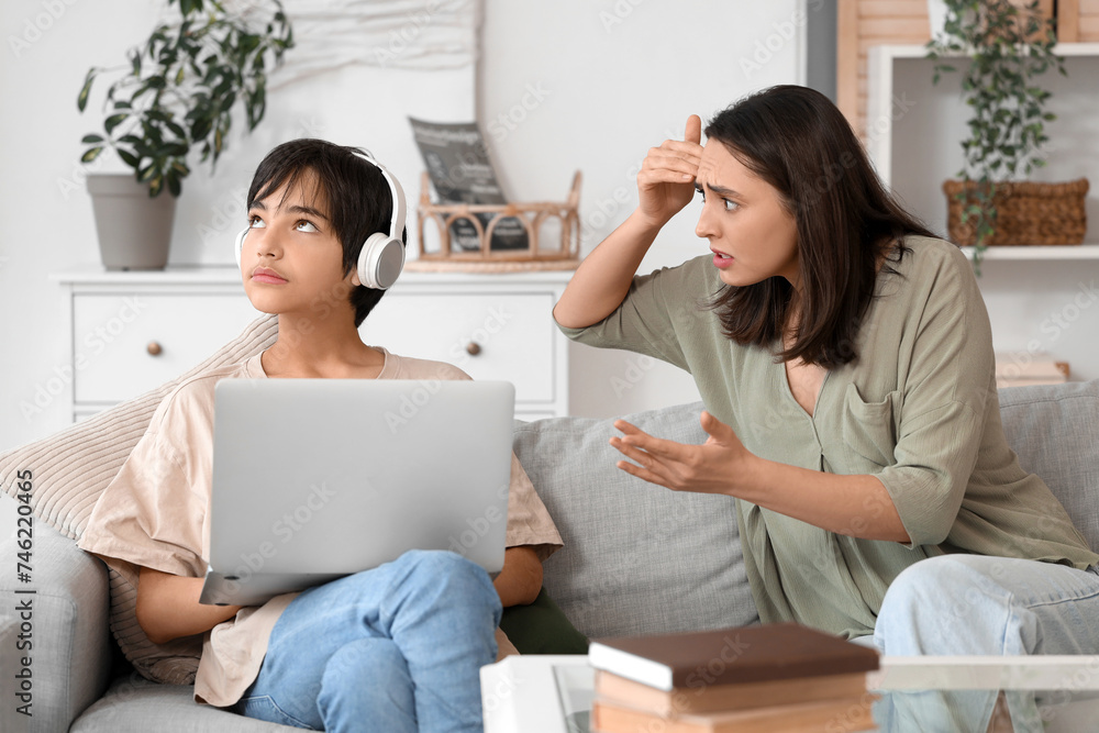 Teenage boy in headphones with laptop ignoring his mother at home. Family problem concept Teenage boy in headphones with laptop ignoring his mother at home. Family problem concept