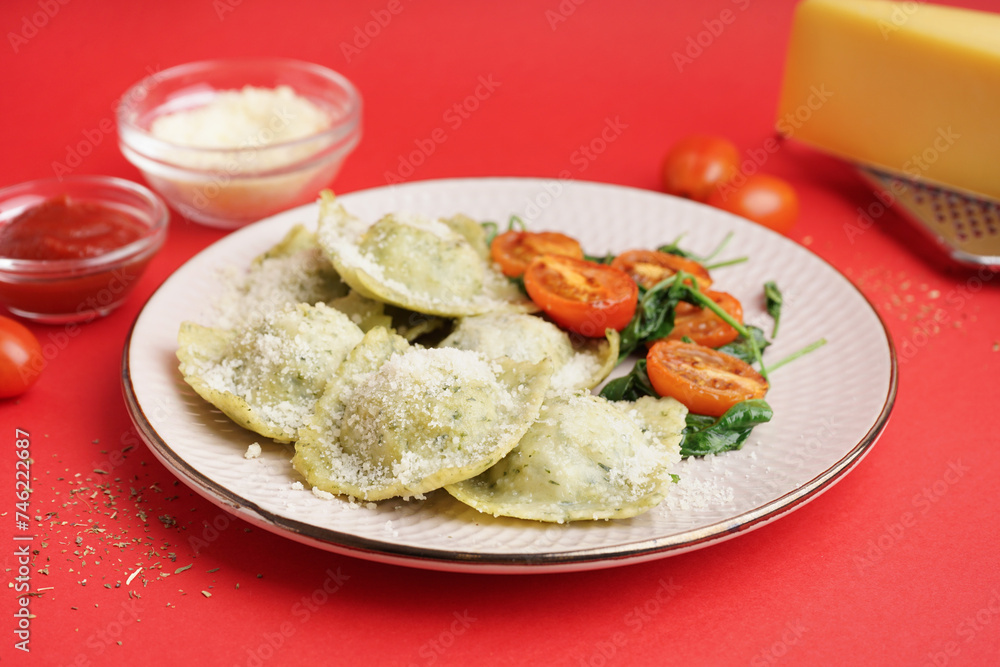 Plate of tasty ravioli with tomatoes and cheese on red background Plate of tasty ravioli with tomatoes and cheese on red background