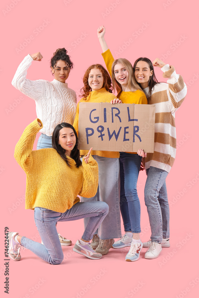 Fototapeta premium Beautiful young happy women holding paper with text GIRL POWER and showing muscles on pink background. Women history month
