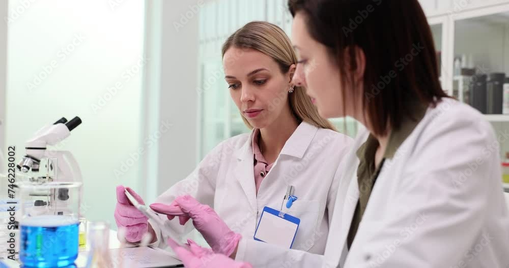Modern research laboratory, two female scientists work with digital tablet and analyze samples of biochemical substances Modern research laboratory, two female scientists work with digital tablet and analyze samples of biochemical substances