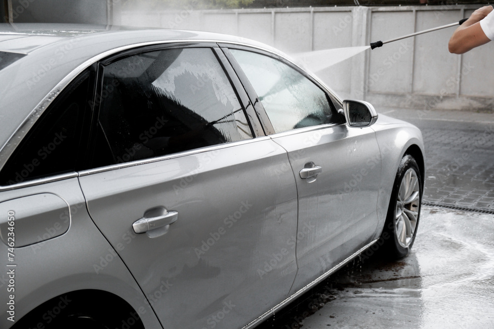 Washing luxury silver car on touchless car wash. Washing sedan car with foam self-service and high pressure water. Cleaning the details of car. Cleanliness and order in urban environment