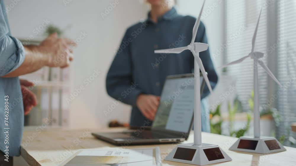 Male and female engineers discussing sustainable energy project during workday in the office, models of wind turbines on table in foreground. Midsection shot Male and female engineers discussing sustainable energy project during workday in the office, models of wind turbines on table in foreground. Midsection shot