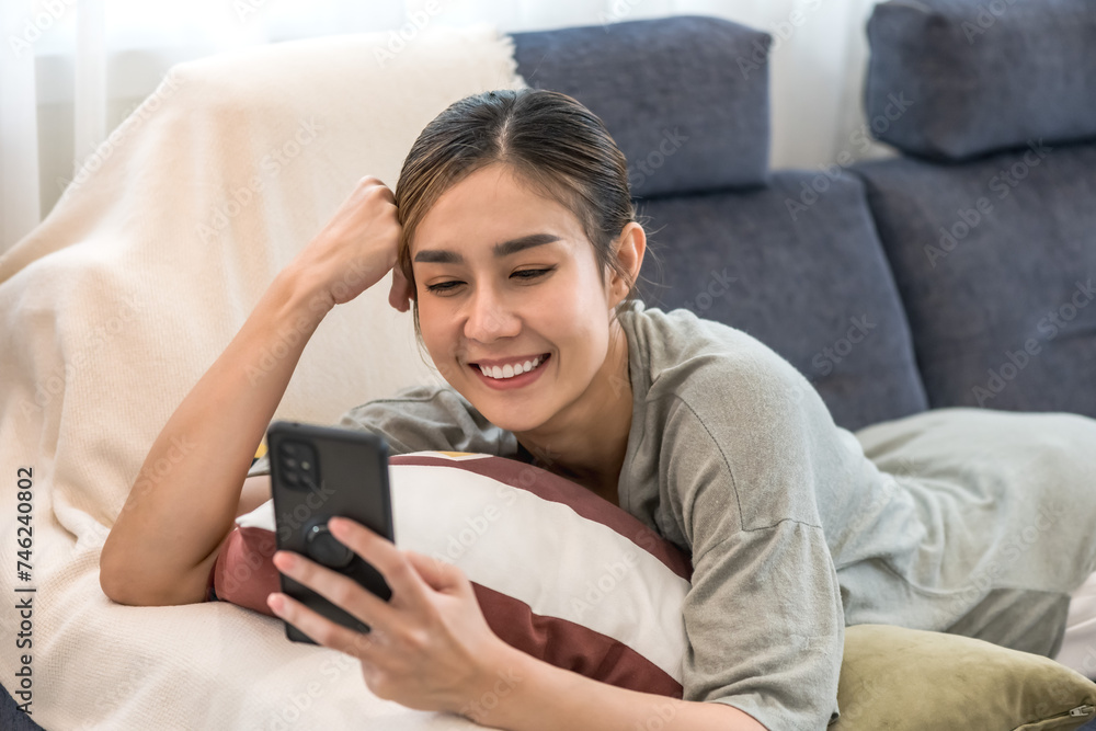 Portrait young Asian woman with casual lifestyle lying on sofa and texting on mobile phone Portrait young Asian woman with casual lifestyle lying on sofa and texting on mobile phone