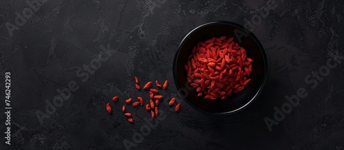 A black bowl filled with vibrant red food sits atop a wooden table. The stark contrast between the dark bowl and bold-colored food creates a visually striking scene.