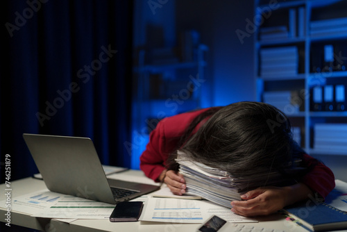 Asian businesswoman is tired, sleepy and bored from sitting at a desk for a long time working on a laptop computer. Problematic financial paperwork Office syndrome concept. photo