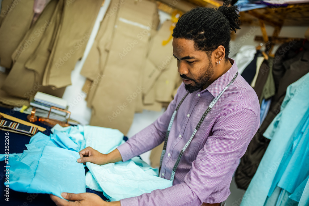 Male African American tailor, in his atelier, folding the fabric. Male African American tailor, in his atelier, folding the fabric.
