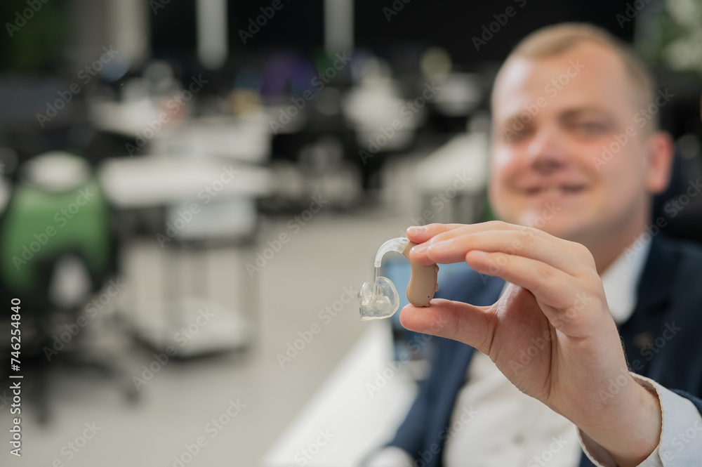 Deaf man working holds hearing aid while sitting in office. Deaf man working holds hearing aid while sitting in office.