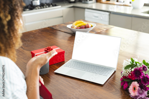 Biracial woman enjoys a surprise gift at home during an online date video call, with copy space