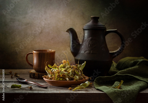 Still life with dried linden blossoms in a plate and linden tea in a teapot on a dark background