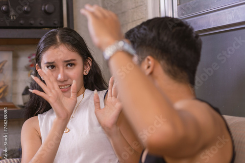 A young woman puts her hands up, trying to protect herself from a slap from her physically abusive boyfriend. photo