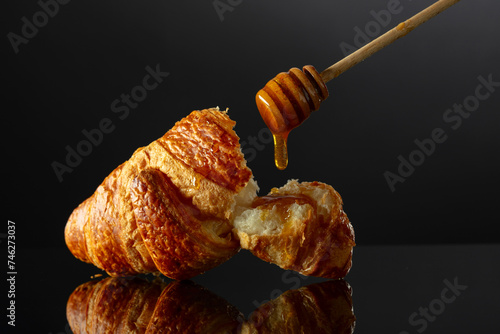 Fresh baked croissant with honey on a black reflective background.