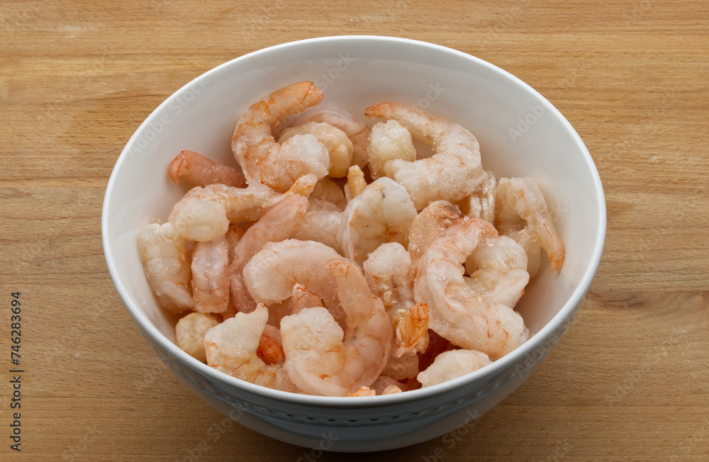 Frozen shrimps in a white bowl, isolated on wooden background Frozen shrimps in a white bowl, isolated on wooden background