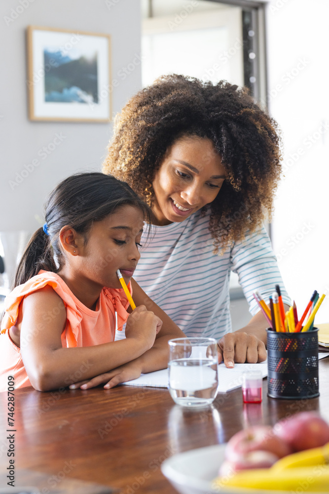 Biracial woman helps her daughter with homework at home Biracial woman helps her daughter with homework at home