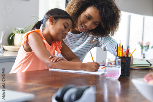 Biracial mother helps a young biracial daughter with homework at home