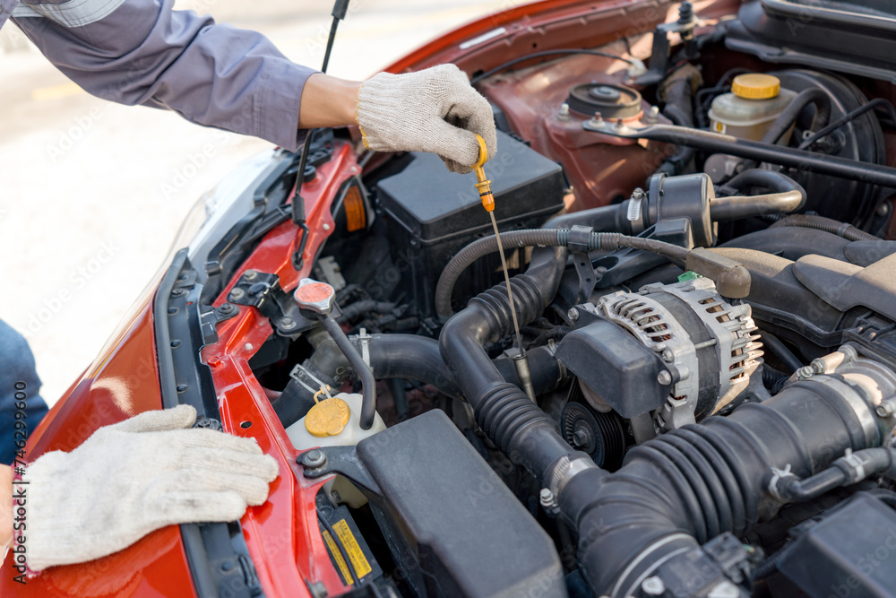 Closeup mechanic hand with protective glove checking the oil level of a car. Routine car maintenance for safe and efficient engine operation. Working atmosphere at car repair shop. Closeup mechanic hand with protective glove checking the oil level of a car. Routine car maintenance for safe and efficient engine operation. Working atmosphere at car repair shop.