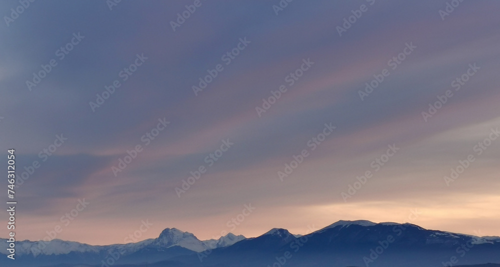 Una coperta di nuvole grige e rosa si stende sopra le cime delle montagne innevate