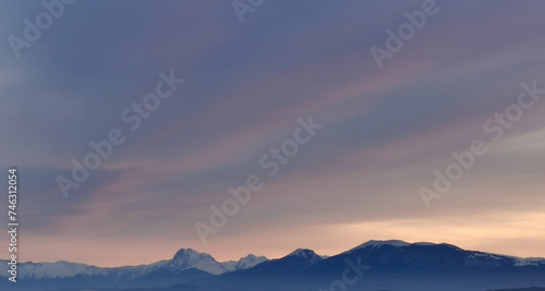 Una coperta di nuvole grige e rosa si stende sopra le cime delle montagne innevate