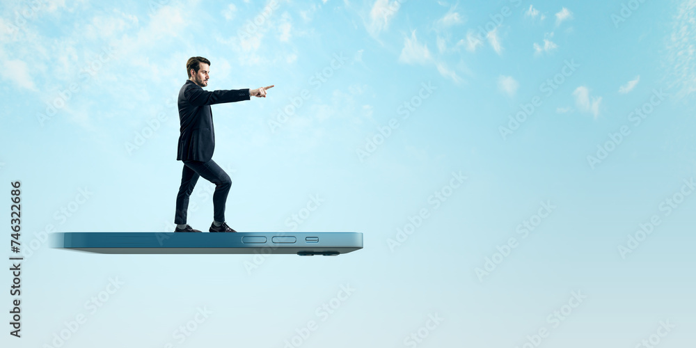 A young man in a business casual outfit balances on a giant smartphone, confidently pointing towards a seemingly endless sky It emphasizes concepts of leadership, innovation, and the digital age